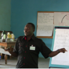 A man at a white board leading a community workshop in Nigeria.