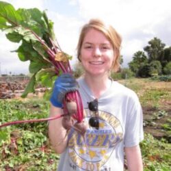 Young blond woman standing in a field of vegetables holding a freshly picked beet