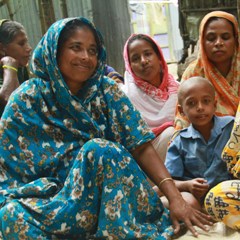 A group of colorfully dressed women and children in a community meeting in Bangladesh.