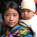 Young Guatemalan girl with baby sister swaddled on her back