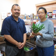 A man and woman standing in a food bank holding fresh vegetables