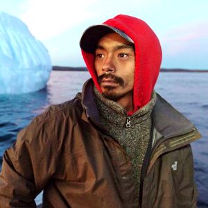 An Inuit fisherman in a boat navigating around an iceberg.