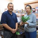 A man and a woman are standing in a food bank and the woman is holding some fresh vegetables